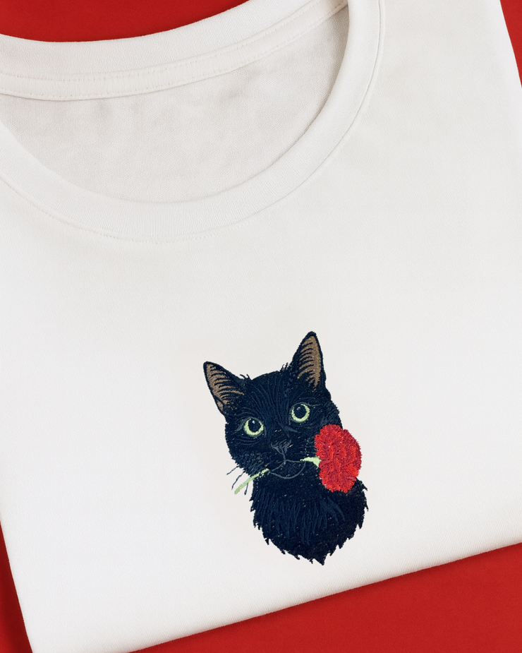 White shirt with black cat embroidered holding a red rose on a red background